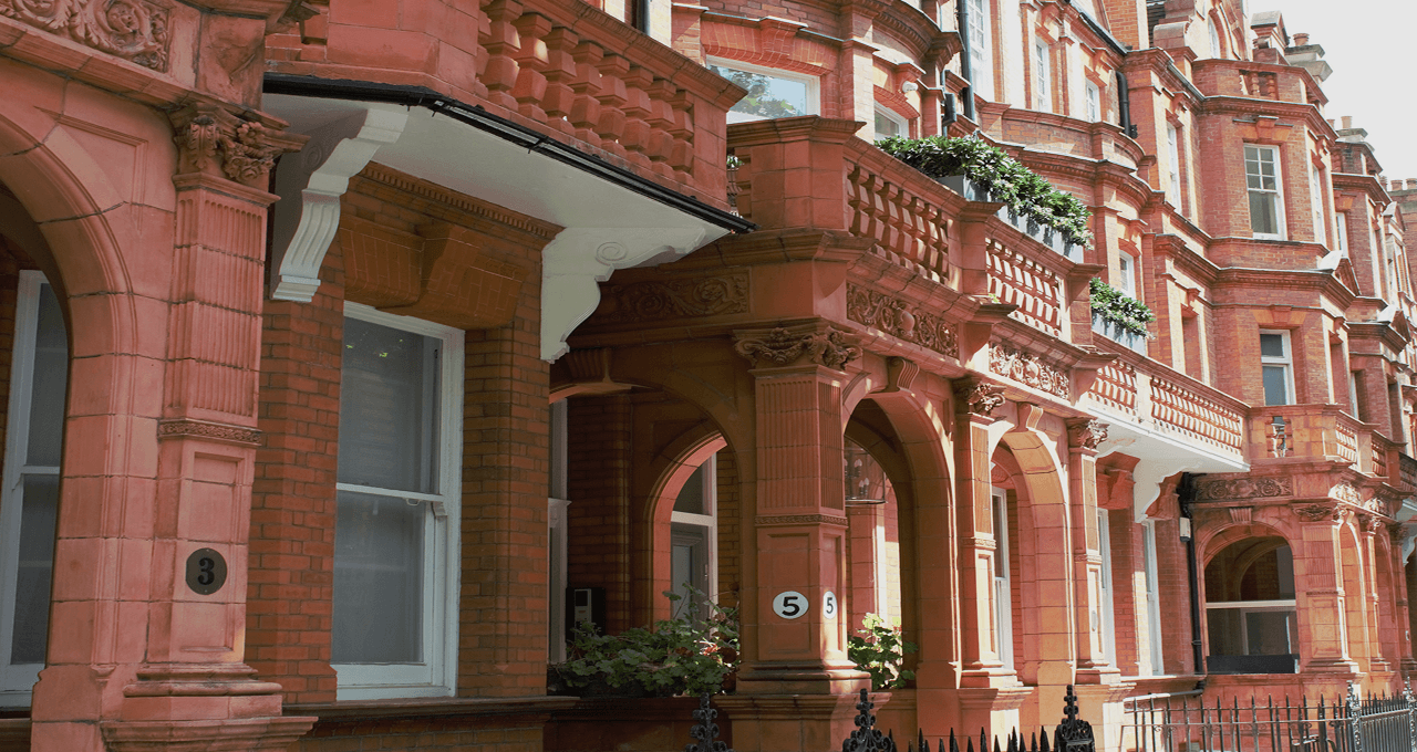 Traditional red-brick residential buildings in a leafy London neighborhood.