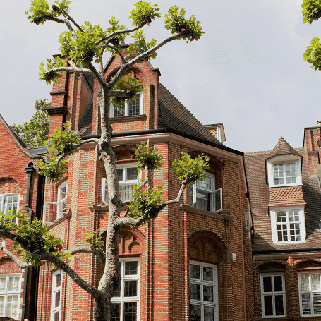 Traditional London townhouse with intricate brickwork and a sculpted tree in front.